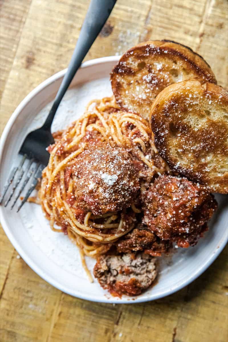 Delicious homemade spaghetti with meatballs and garlic bread on a rustic wooden table.