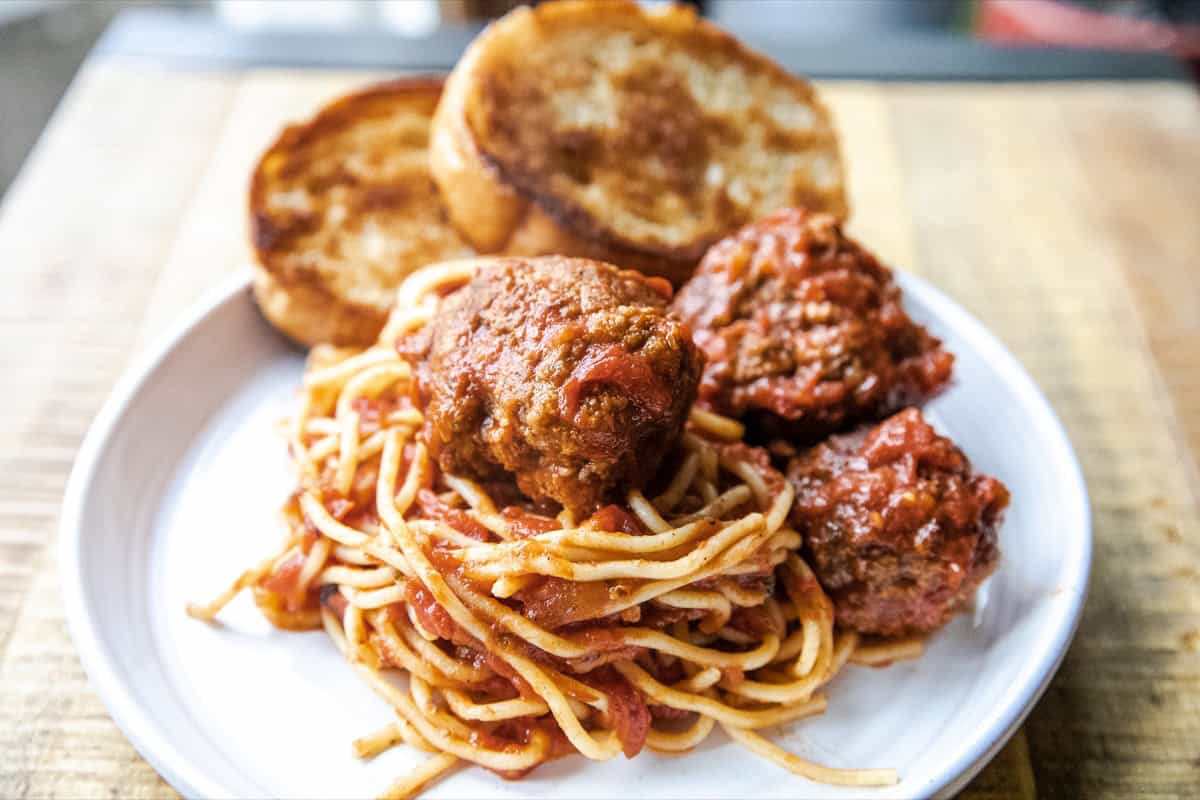 Delicious homemade spaghetti with savory meatballs and garlic bread on a white plate. Perfect comfor.