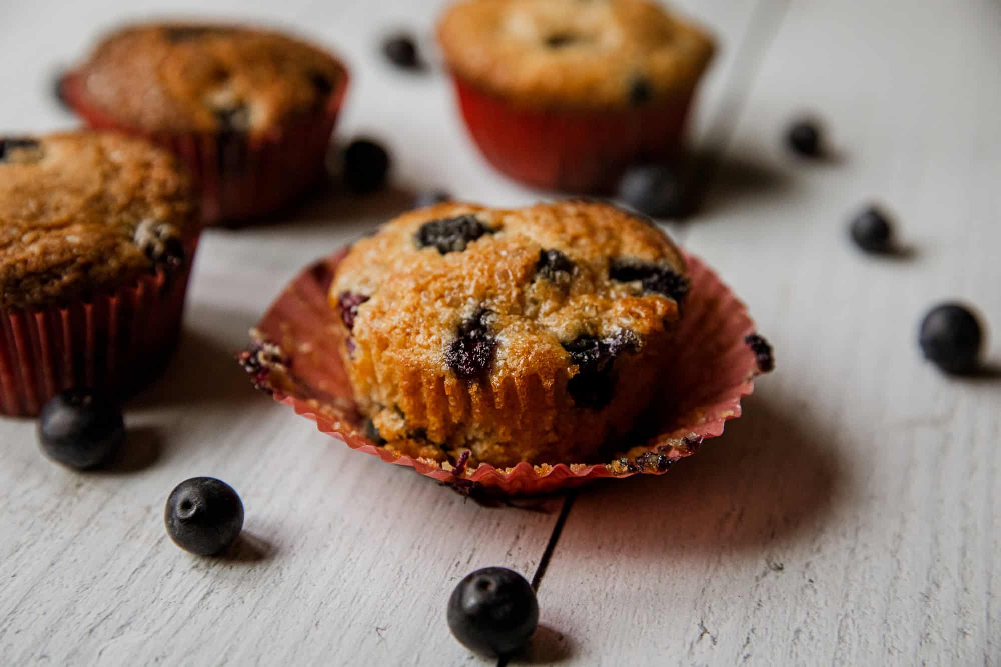 Fresh blueberry muffins in red paper liners with blueberries scattered around.