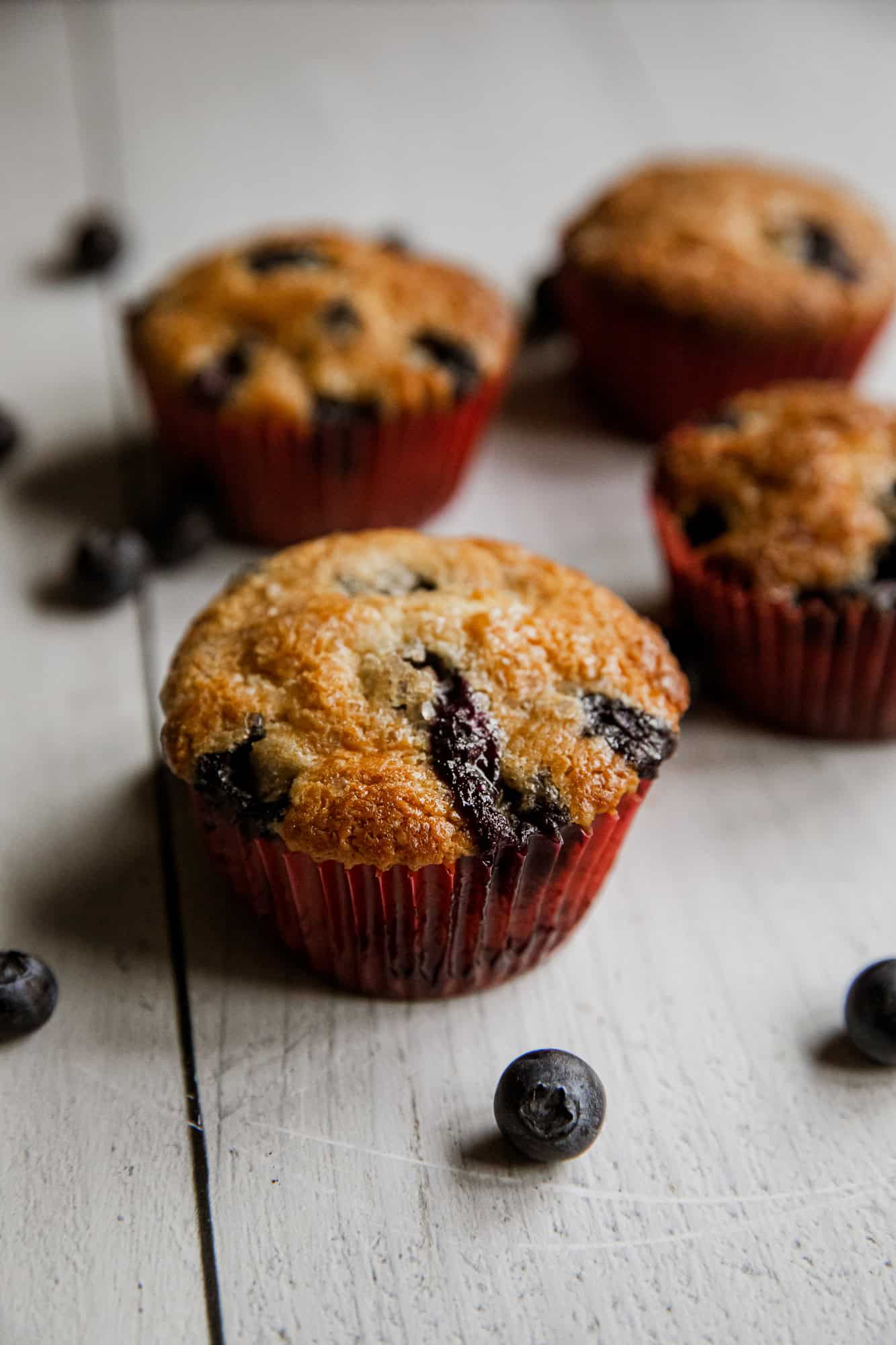 Freshly baked blueberry muffins in red paper cups with blueberries around.