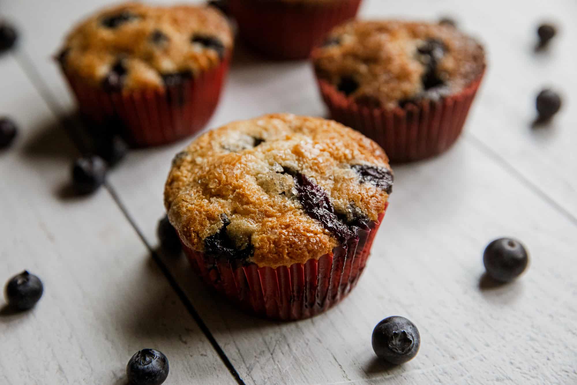 Freshly baked blueberry muffins in red paper liners with blueberries around.