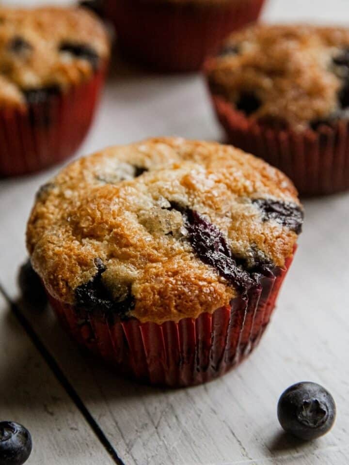 Freshly baked blueberry muffins in red paper liners with blueberries nearby.
