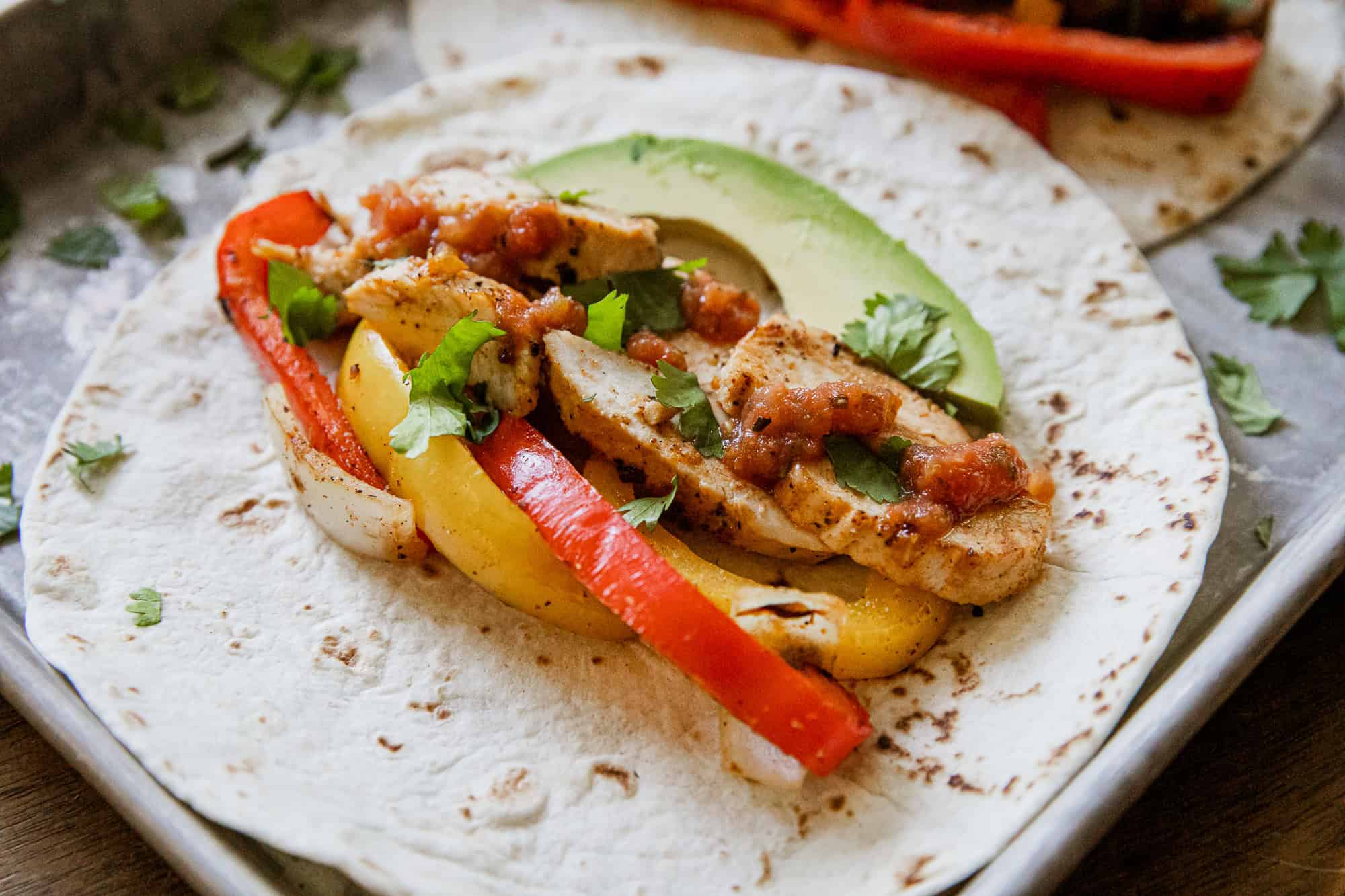 Chicken fajita wrap with colorful peppers, avocado, and fresh herbs on a soft tortilla.