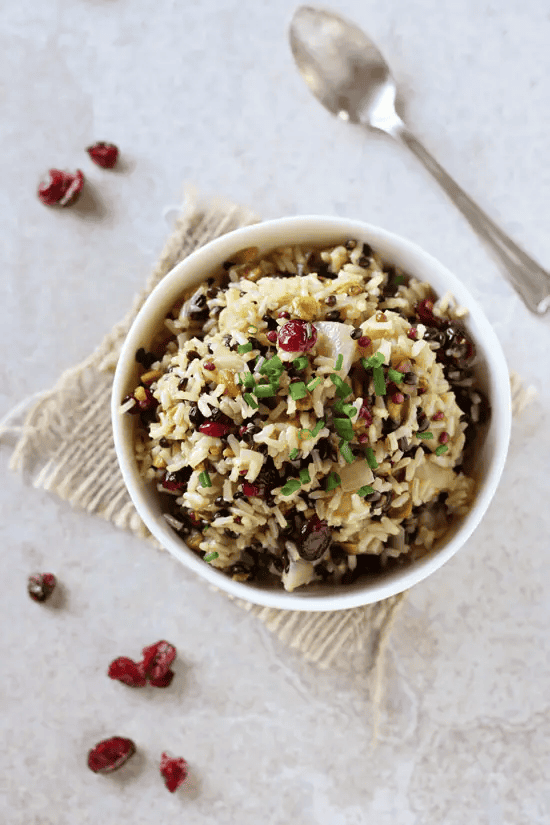 Bowl of wild rice salad with cranberries and herbs on a light background.