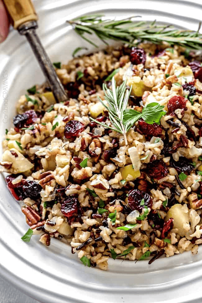 Healthy wild rice salad with cranberries, nuts, and fresh herbs on a white plate.