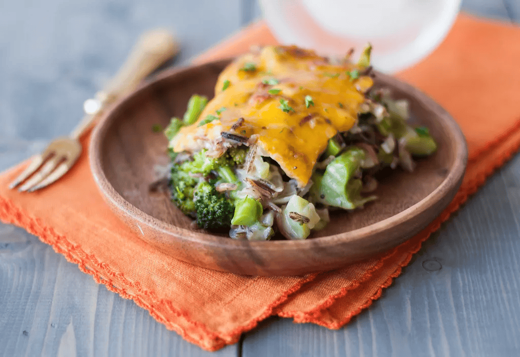 Wild rice casserole with broccoli, mushrooms, and cheese on a wooden plate.