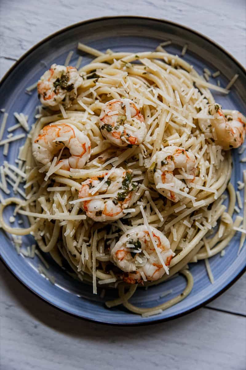 Delicious shrimp scampi pasta with herbs on a blue plate.