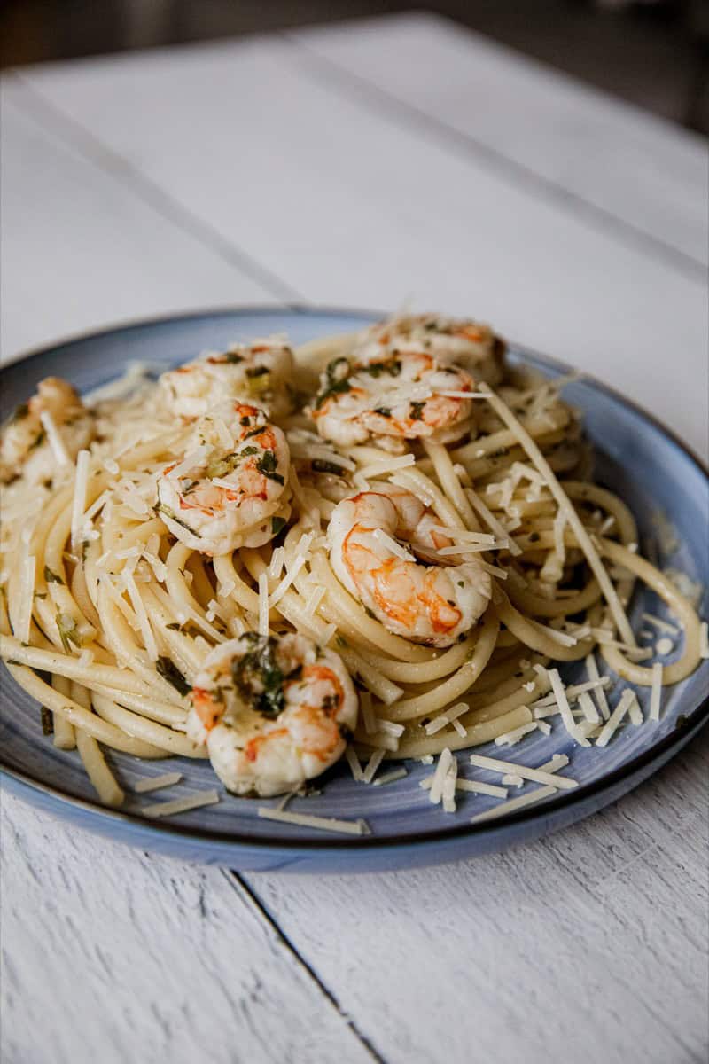 Delicious shrimp scampi pasta served on a blue plate with grated cheese.