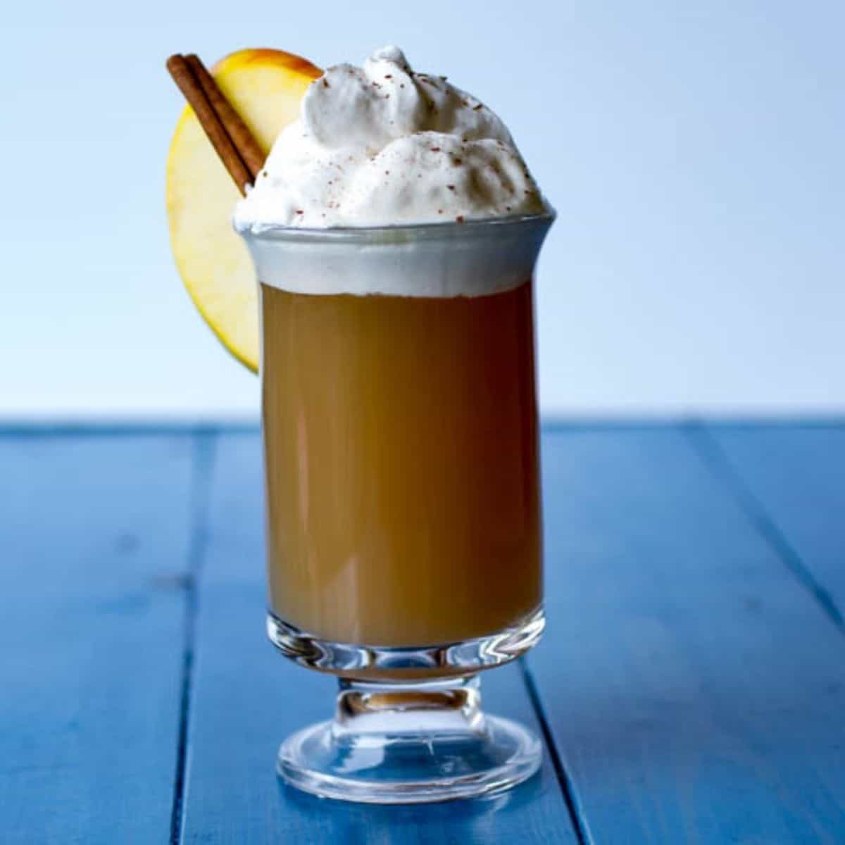 Apple cider with whipped cream, cinnamon, and apple slice garnish.