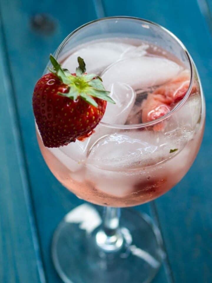 Glass of strawberry white wine spritzer with ice and strawberry garnish.