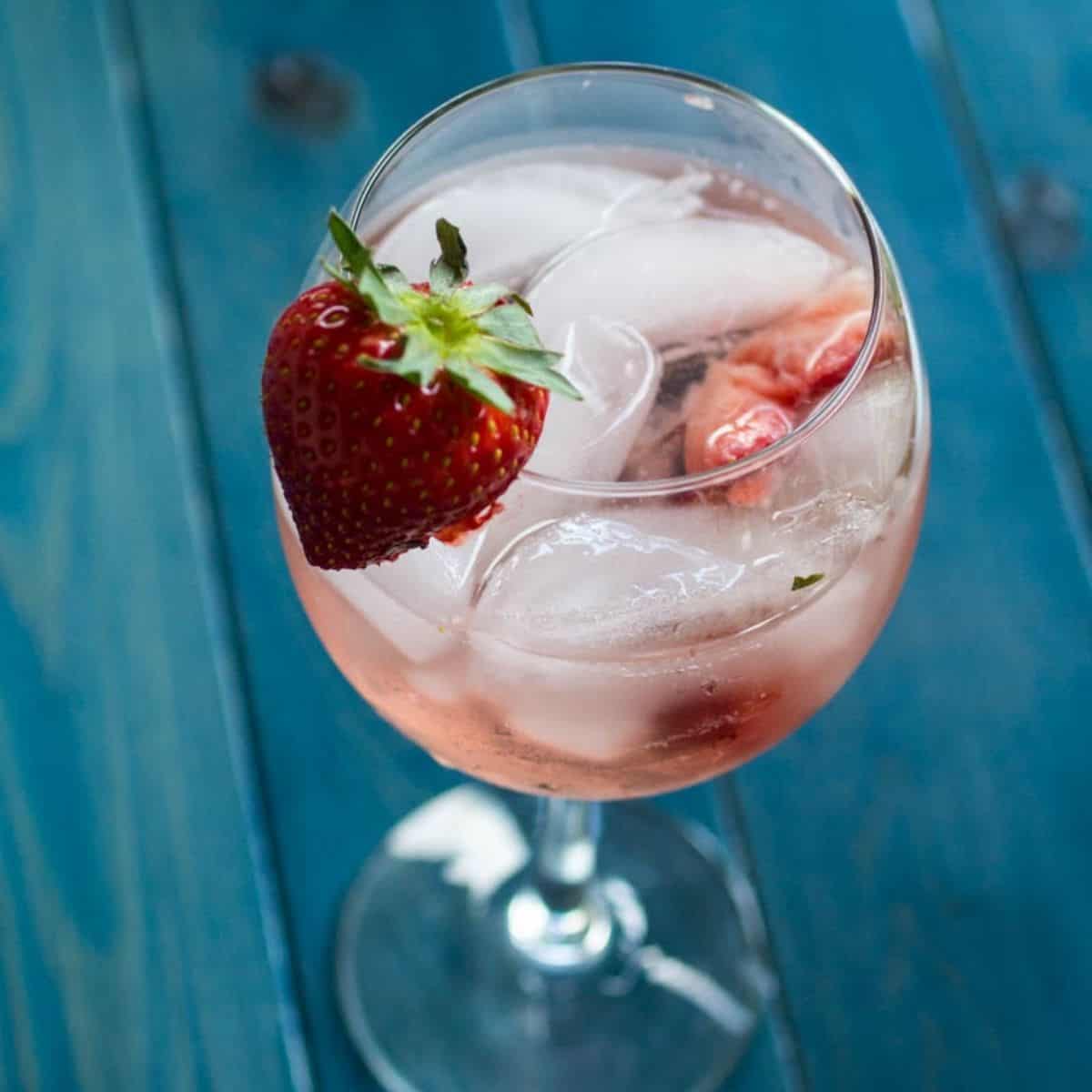Glass of strawberry white wine spritzer with ice and strawberry garnish.