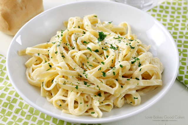 Homemade Alfredo Sauce over linguini in a white bowl on a nicely decorated table