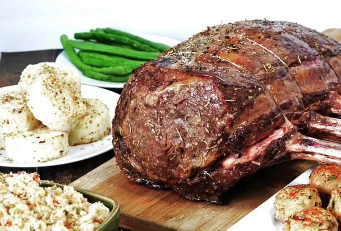 Prime Rib Roast cooked perfectly on a cutting board in the middle of a table full of food.