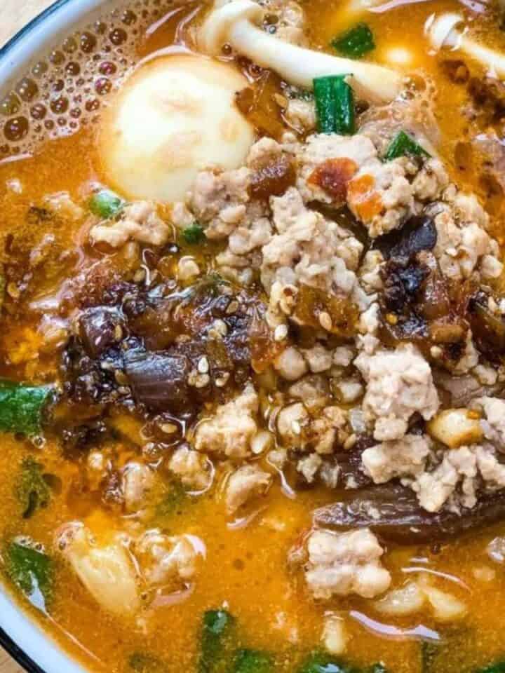 Spicy ramen noodle soup with ground meat, eggs, and vegetables in a flavorful broth.