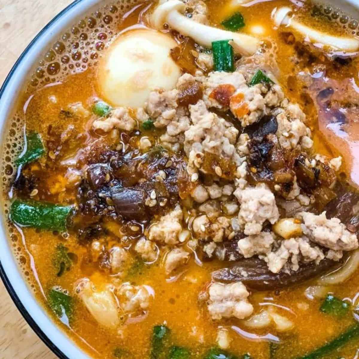 Spicy ramen noodle soup with ground meat, eggs, and vegetables in a flavorful broth.