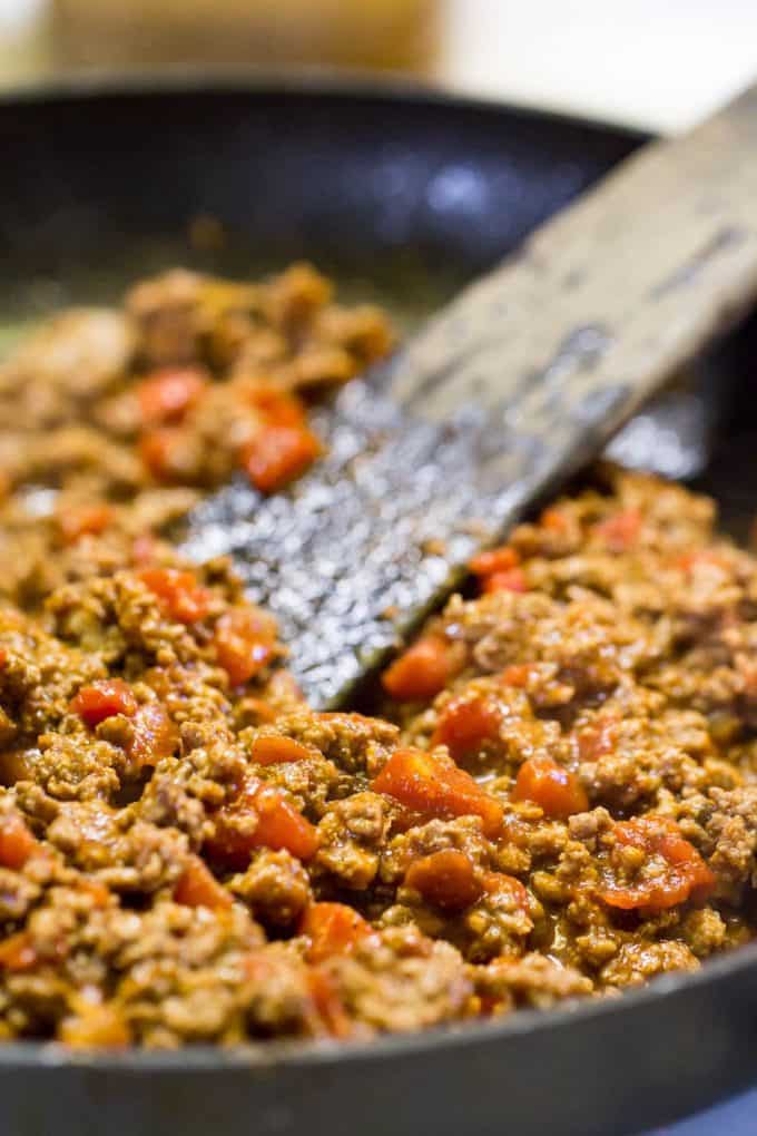 Taco Meat for Pizza browning in a skillet with a wooden spatula in the pan