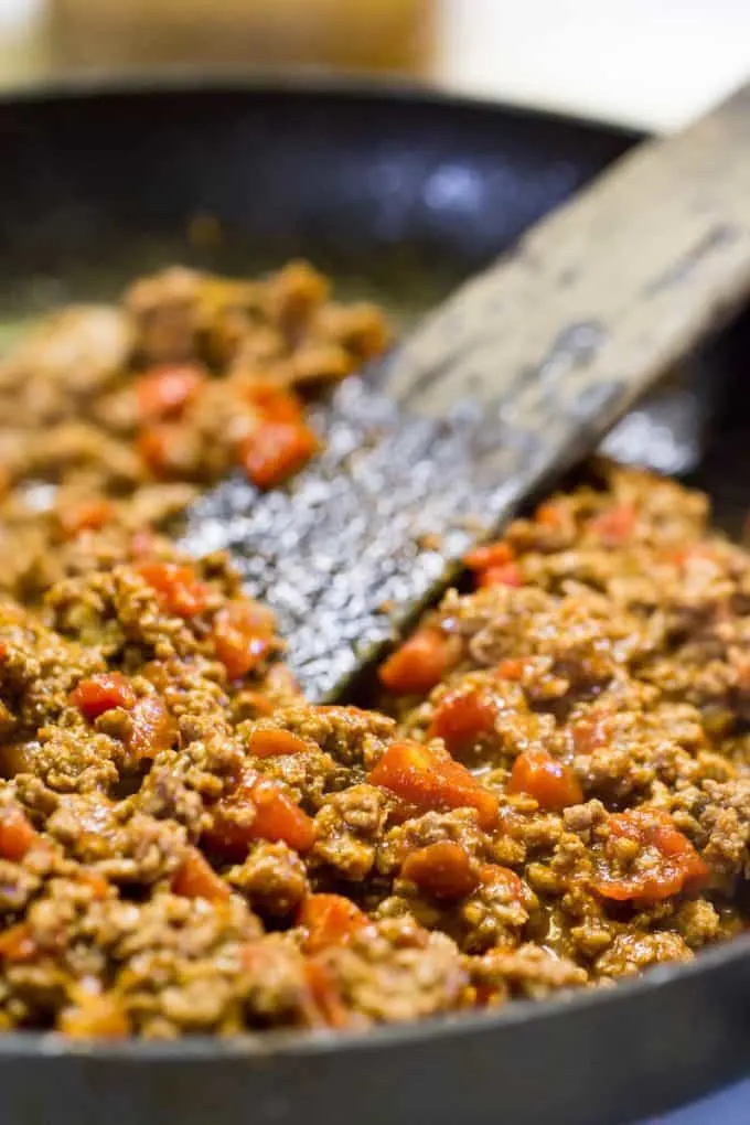 Taco Meat for Pizza browning in a skillet with a wooden spatula in the pan