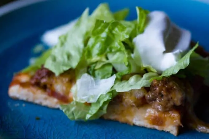 Taco pizza on blue plate with lettuce and sour cream