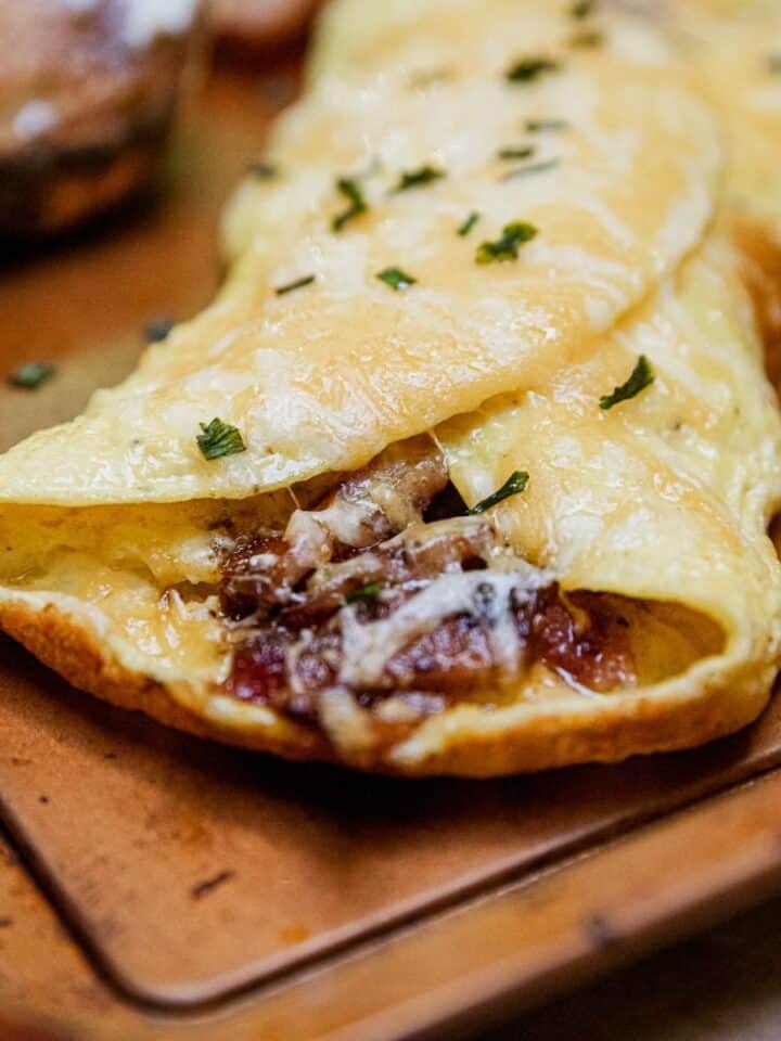 Delicious cheesy beef omelette garnished with herbs on a wooden serving board.