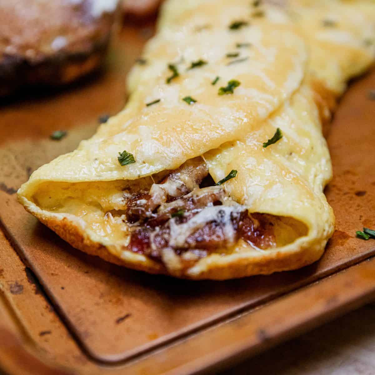 Delicious cheesy beef omelette garnished with herbs on a wooden serving board.