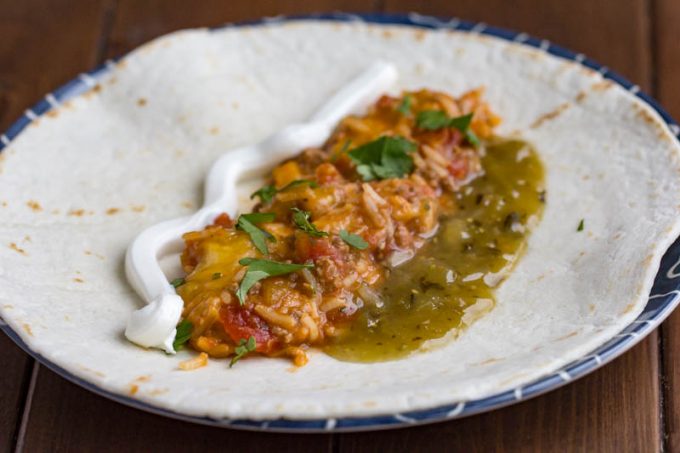 Easy beef and bean burrito skillet with sour cream and salsa verde on a tortilla, unrolled.