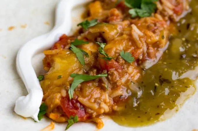 Simple beef and bean burrito skillet close up showing sour cream, chopped cilantro on top, and salsa verde