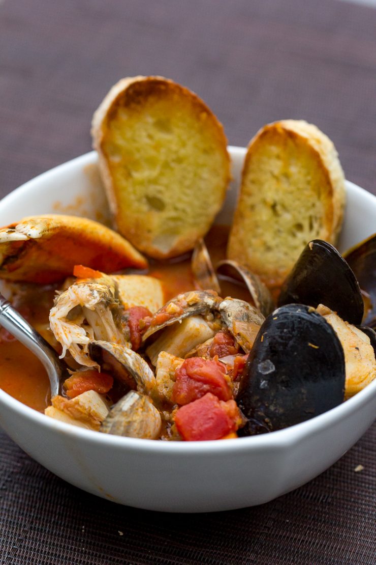 Traeger Pacific Northwest Cioppino with clams, mussels, spot prawns, crab, lingcod, and the most delicious broth! In a white bowl with toasted rounds of baguette.