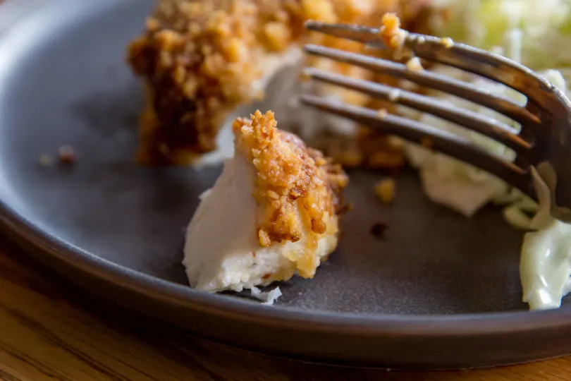 Air Fryer Parmesan Crusted Halibut on a gray plate being cut into with a fork.