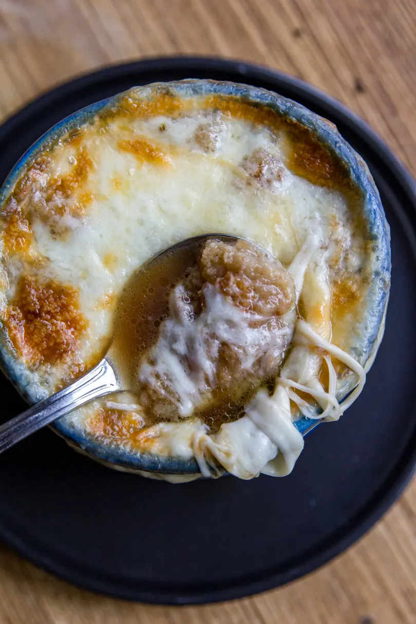 From the top view of a blue bowl of French Onion Soup with a spoon slightly sunken into the bowl on top of the cheese, and bread and cheese on a portion of the spoon.