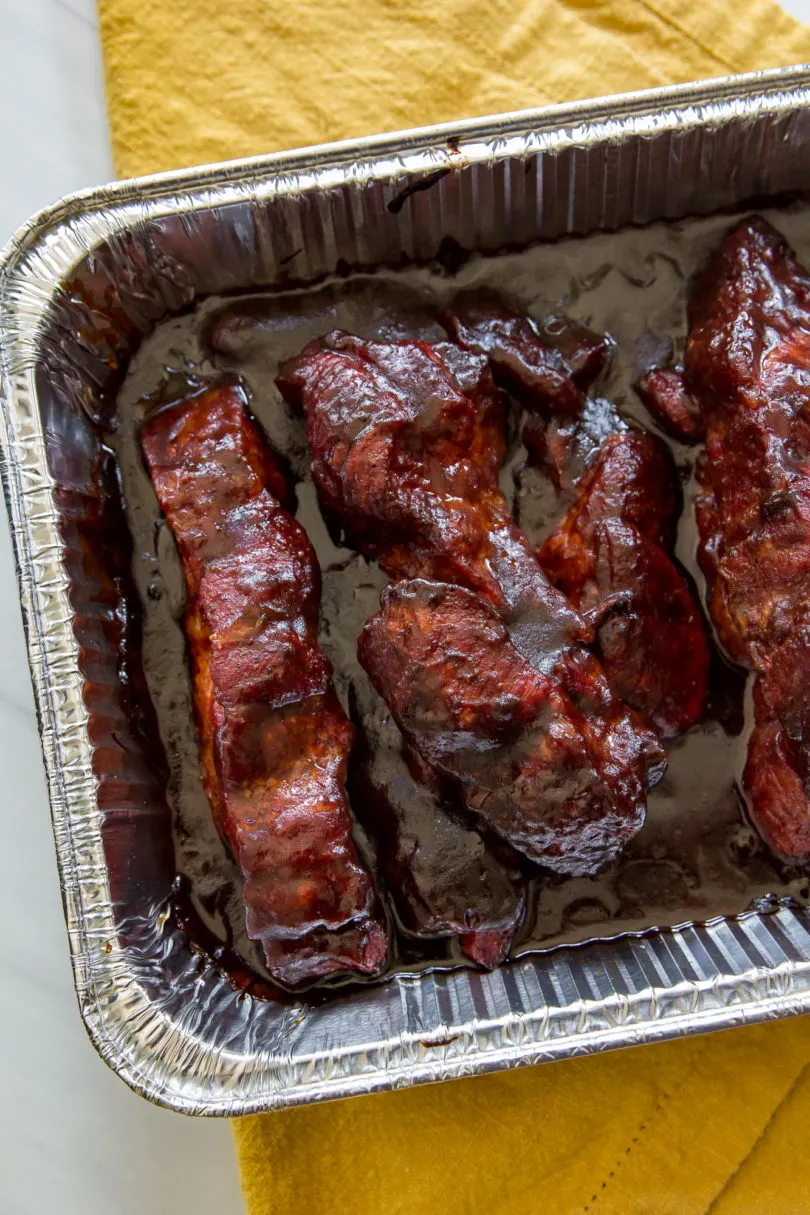 Smoked Country-Style Pork Ribs, top down view, in a foil pan with bbq sauce and the pan is placed on a yellow cloth napkin