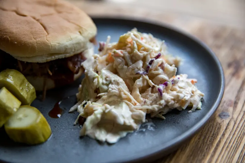 Creamy Coleslaw on a plate with pickles and a sandwich