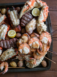 Shrimp and Scallop Skewers on a large baking sheet with steak, lobster tails, sliced lemons, small potatoes, and giant crab legs