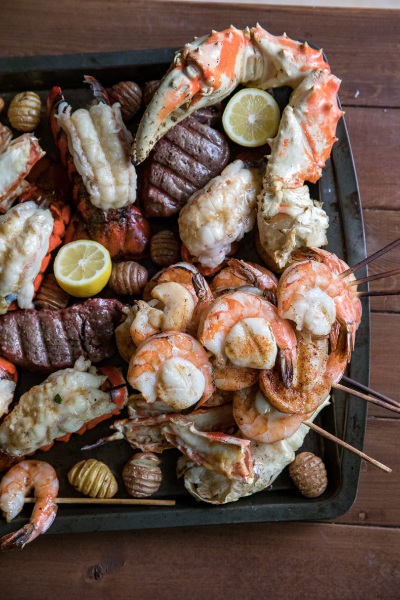 Shrimp and Scallop Skewers on a large baking sheet with steak, lobster tails, sliced lemons, small potatoes, and giant crab legs