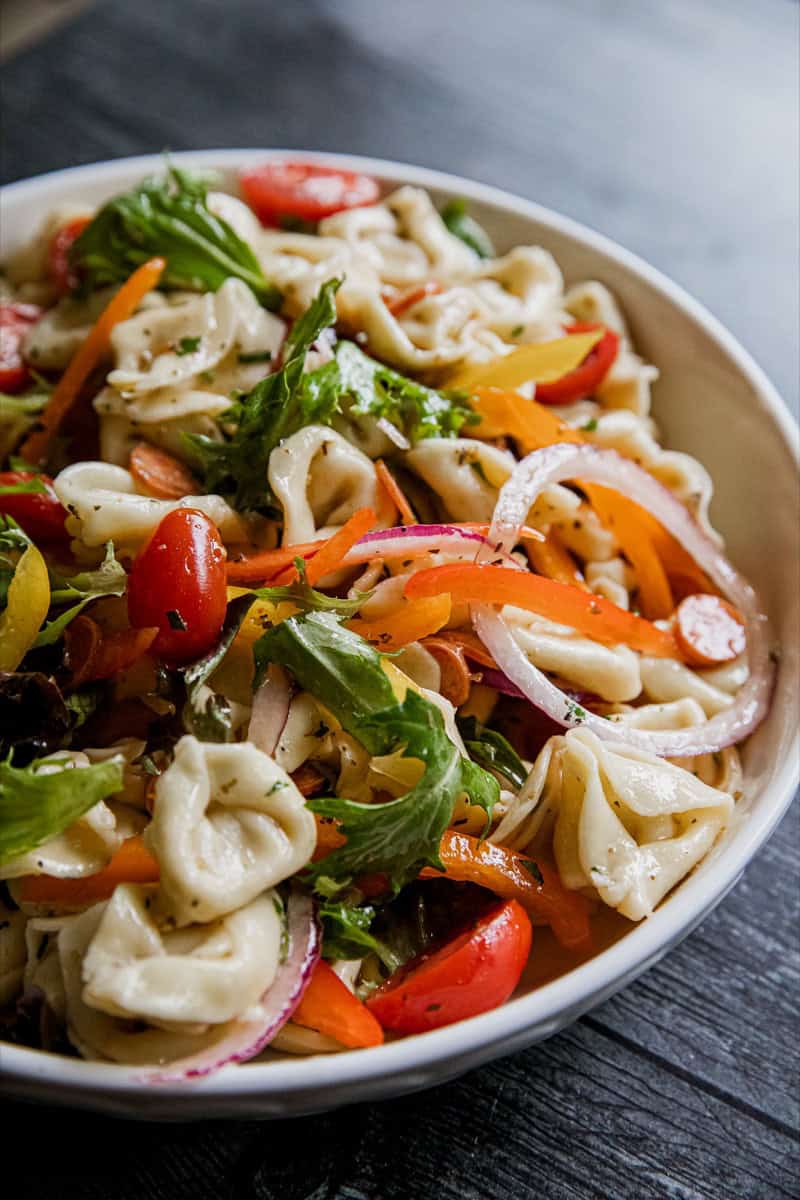 Colorful tortellini pasta salad with vegetables and herbs in a white bowl.