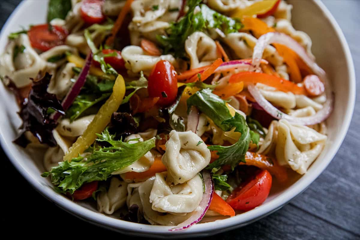 Colorful tortellini pasta salad with vegetables in a white bowl.