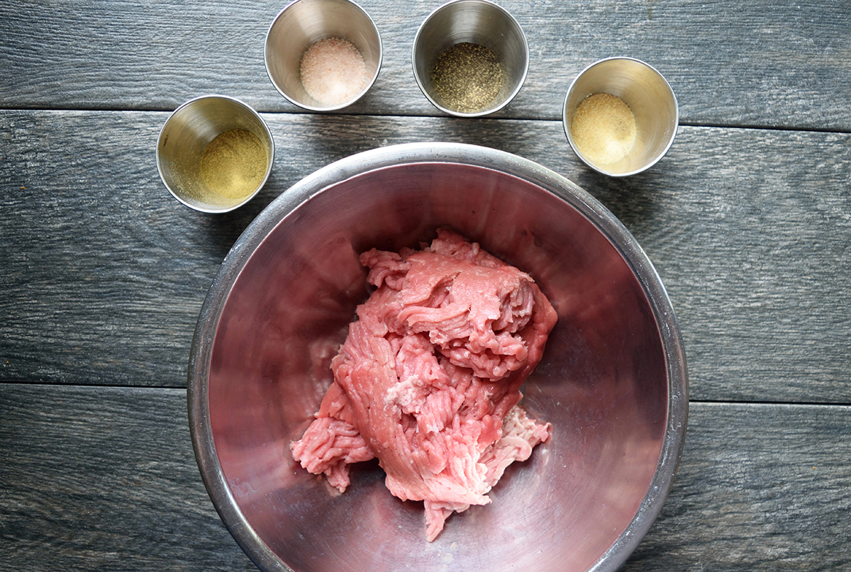 A bowl of seasoned ground meat on a wooden table.