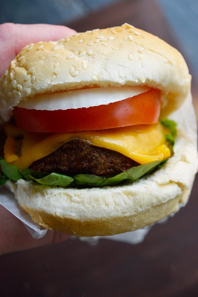 A person holding a mouthwatering air fryer turkey burger topped with cheese and tomatoes.