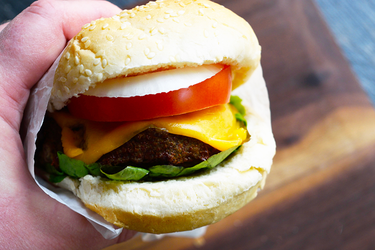 A person holding a burger topped with cheese and tomatoes, cooked using an air fryer.