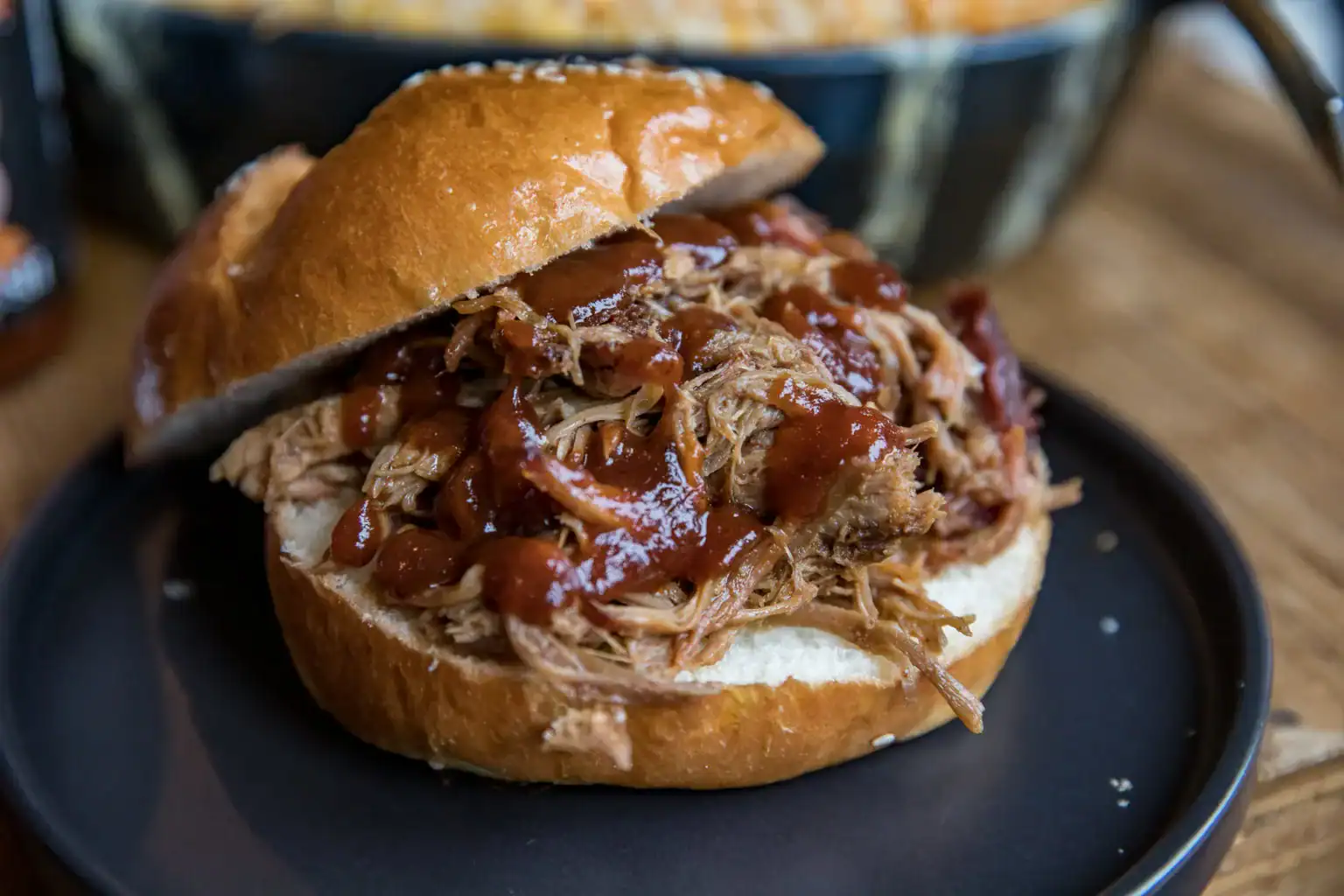 Juicy pulled pork sandwich with barbecue sauce in a soft bun, served on a black plate.