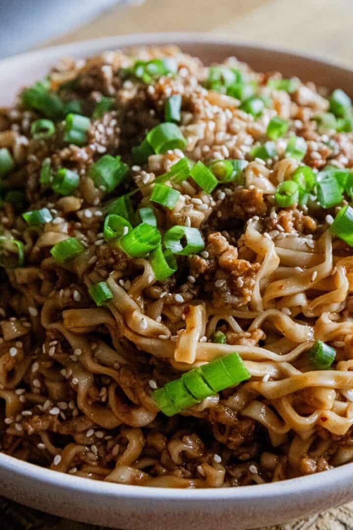 Close-up of soy scallion noodles with pork garnished with green onions in a white bowl.