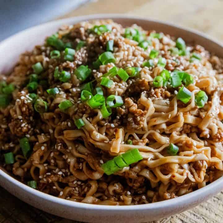 Close-up of soy scallion noodles with pork garnished with green onions in a white bowl.