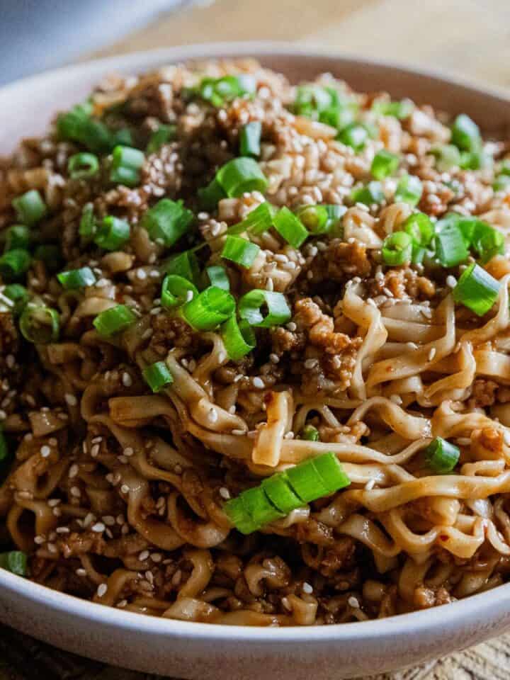 Close-up of soy scallion noodles with pork garnished with green onions in a white bowl.