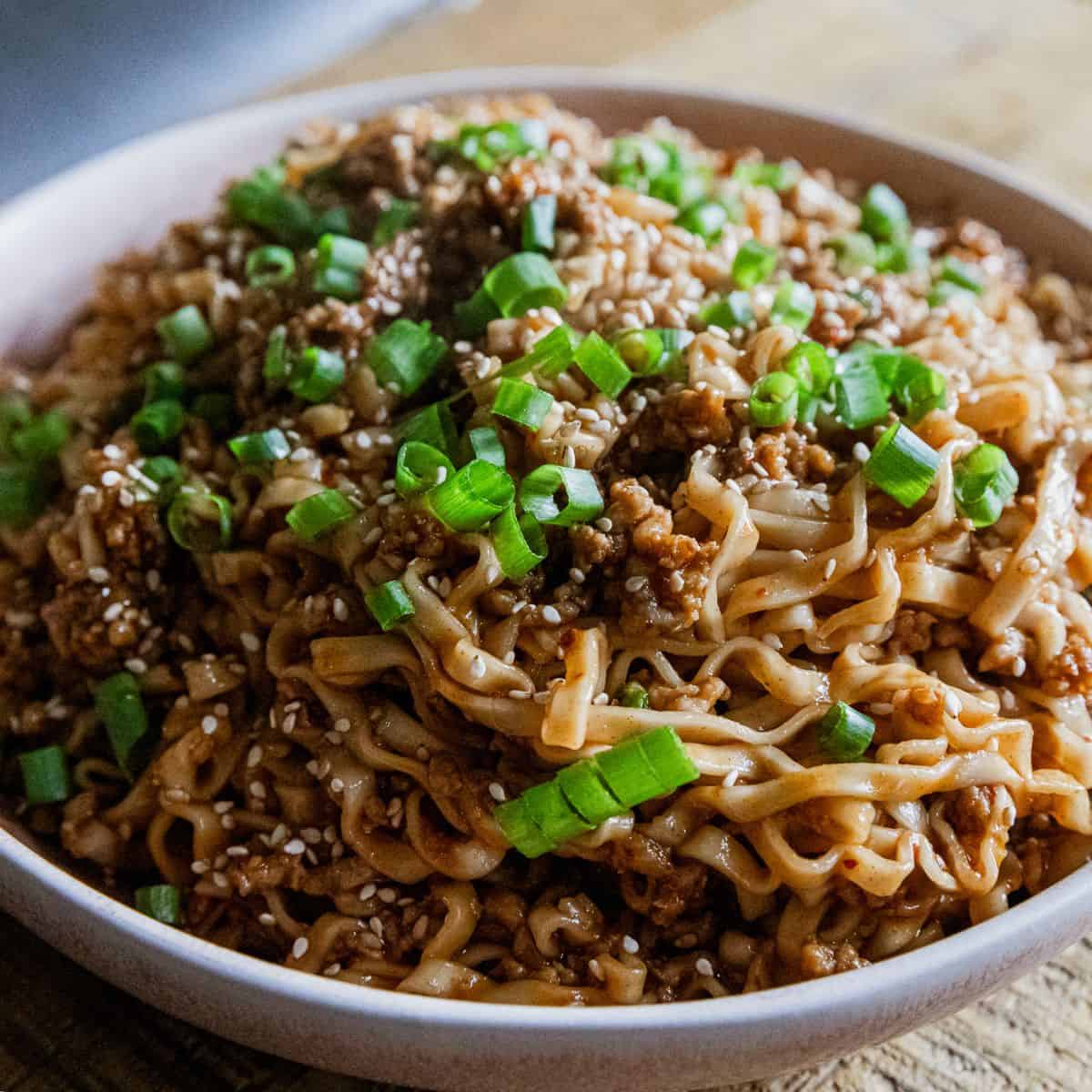 Close-up of soy scallion noodles with pork garnished with green onions in a white bowl.