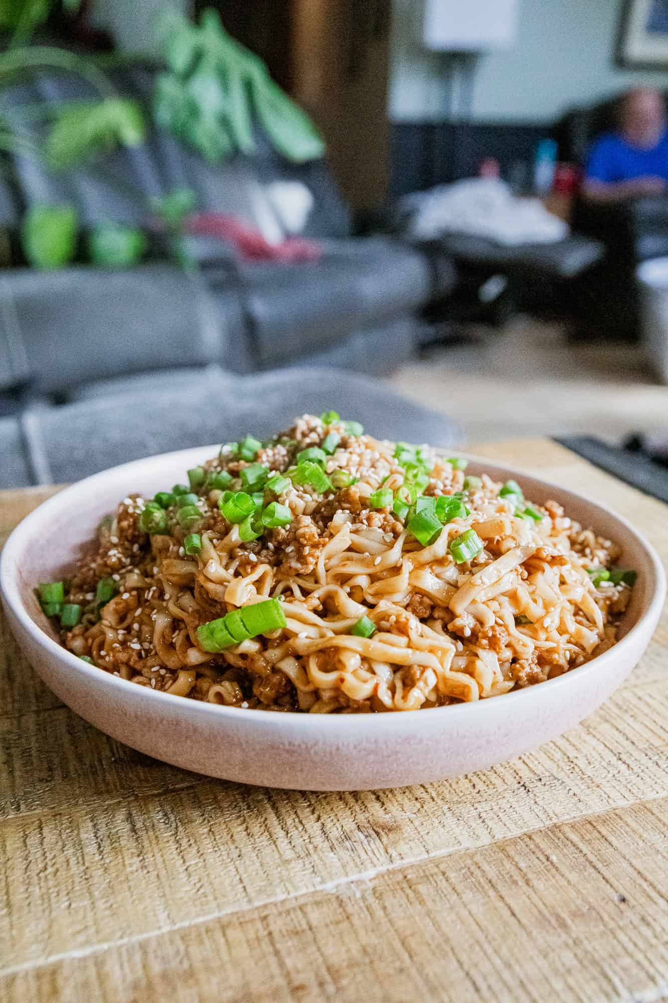 Soy scallion noodles with pork in a white bowl, garnished with chopped green onions.