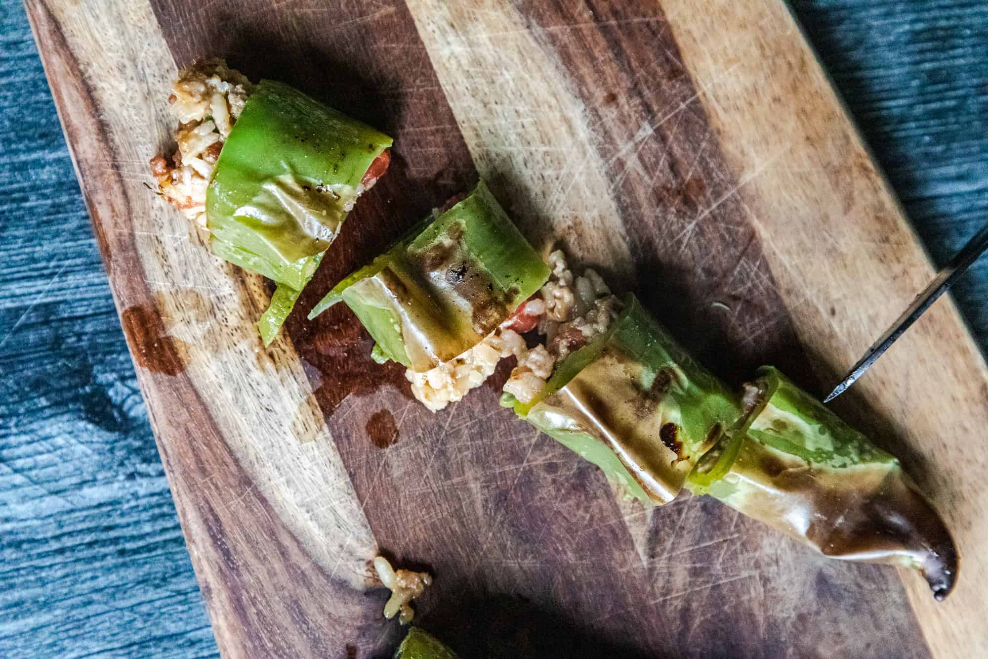 Spicy stuffed hatch chili peppers with cheese and savory filling on a wooden cutting board.