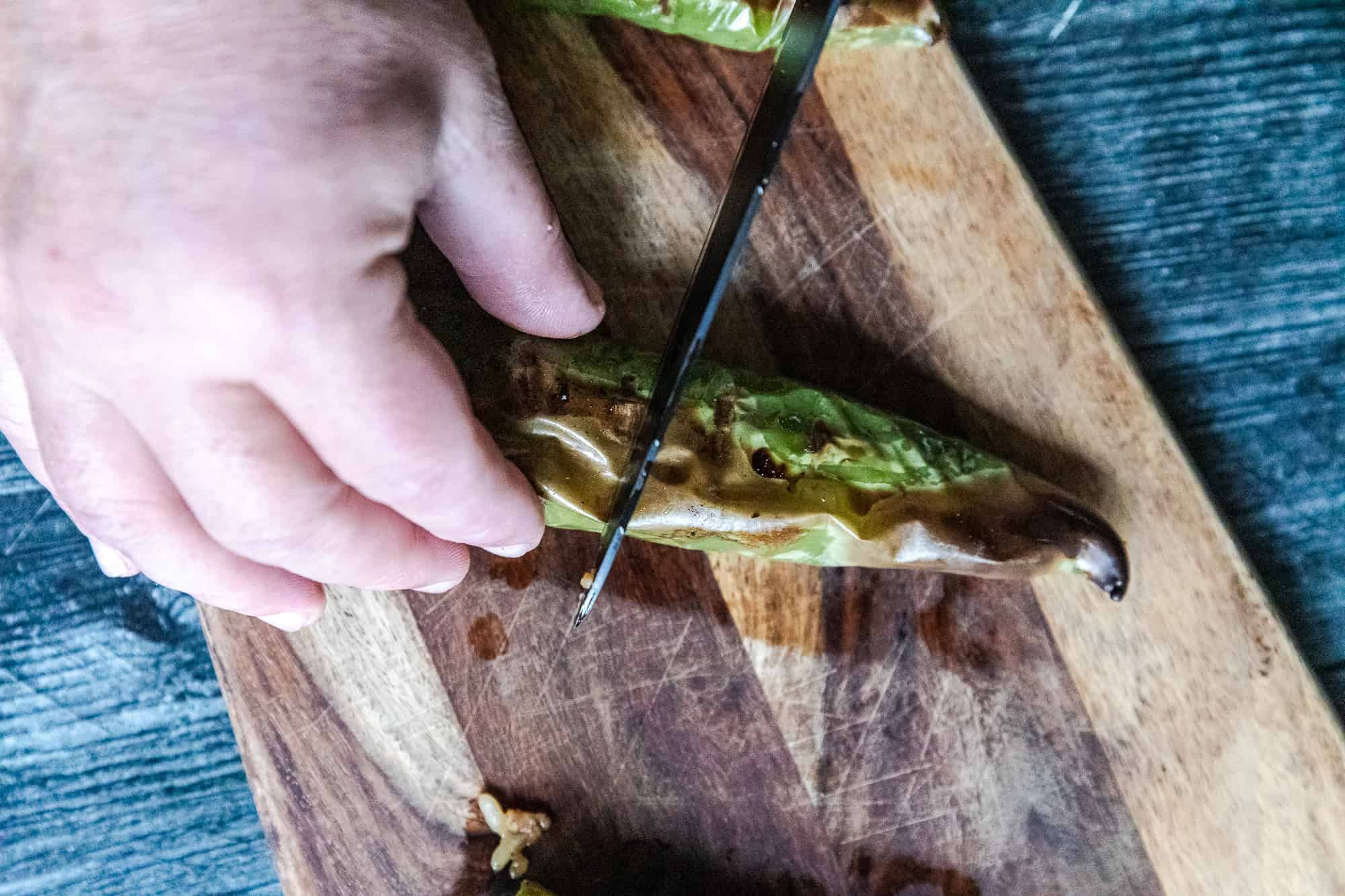 Cutting into spicy grilled Hatch chili peppers on a wooden cutting board.