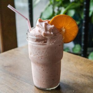 Refreshing strawberry orange Julius Ninja Slushi in a glass with a slice of orange.