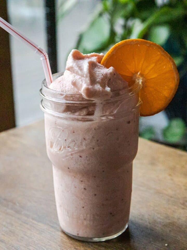 Refreshing strawberry orange Julius Ninja Slushi in a glass with a slice of orange.