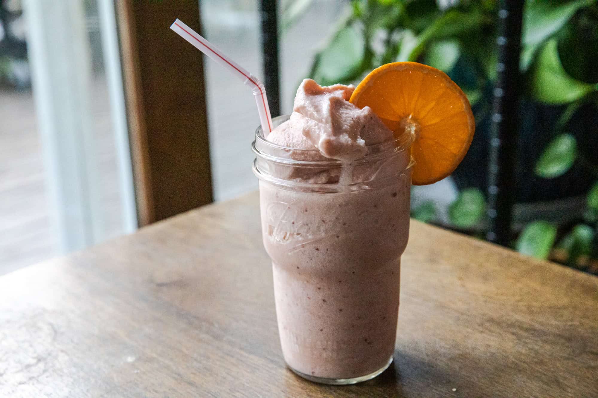 Refreshing strawberry orange Julius Ninja Slushi in a glass with whipped topping and orange slice.