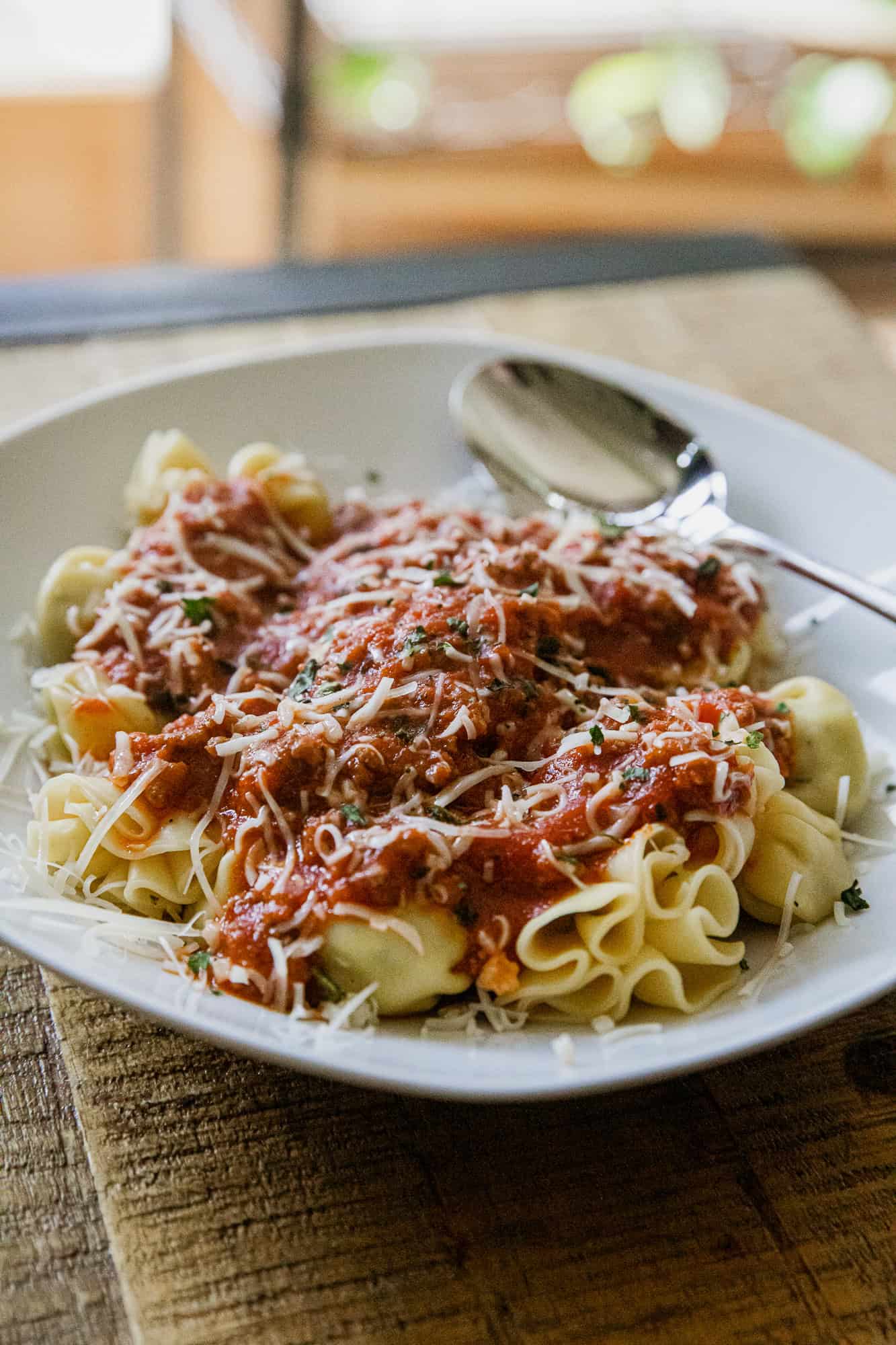 Delicious cheese tortellini topped with savory meat sauce, garnished with grated cheese, served on a.